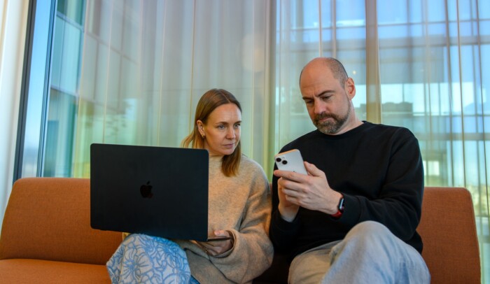 Tv&aring; personer sitter i en soffa och kollar p&aring; en dator och en mobiltelefon.