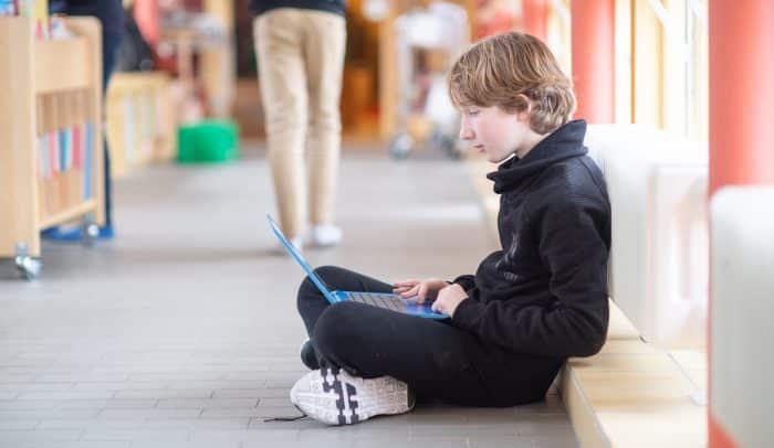 Elev i mellanstadie&aring;lder sitter p&aring; golvet i skolmilj&ouml; och anv&auml;nder en dator.